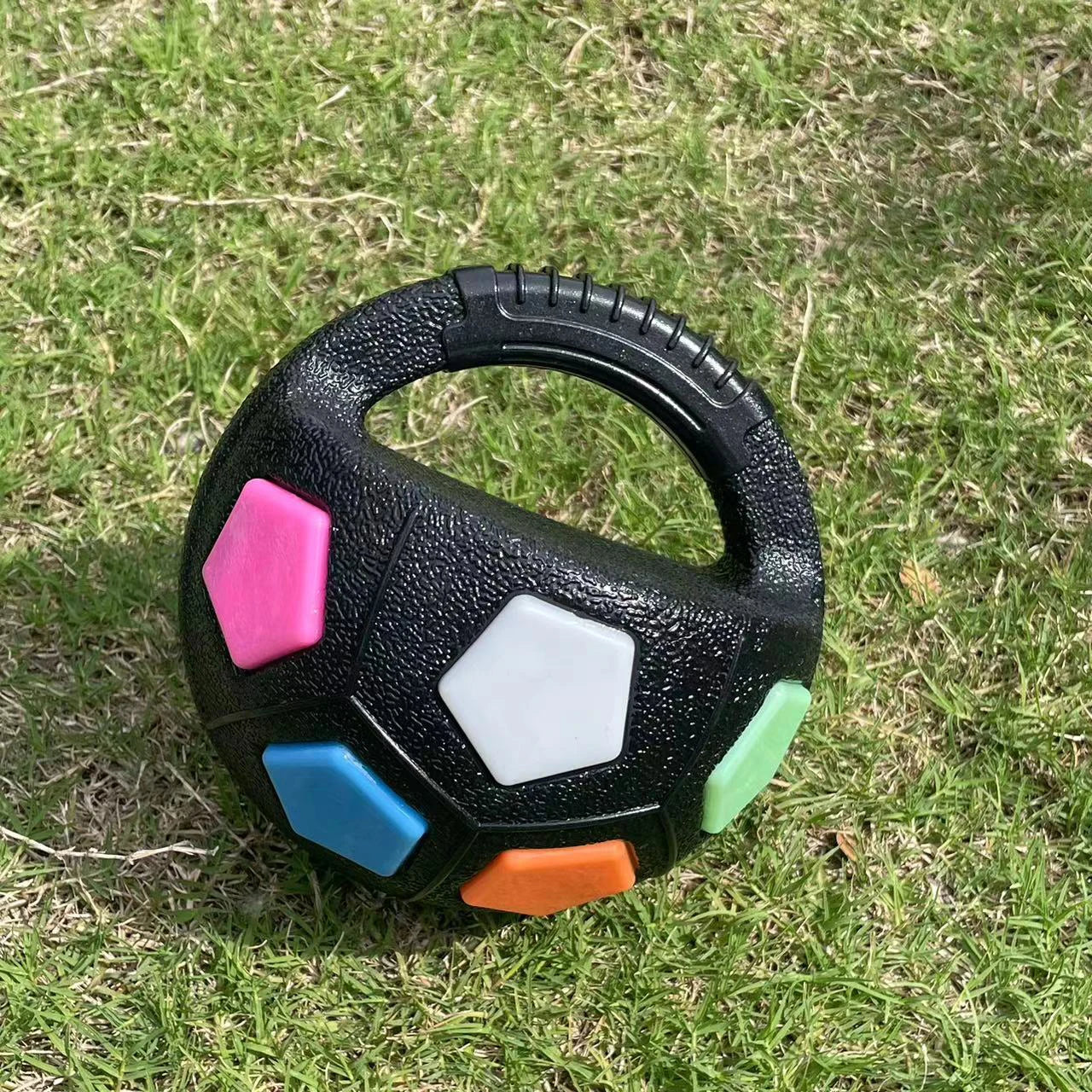 Le ballon noir aux motifs colorés repose sur l’herbe, prêt pour le jeu.