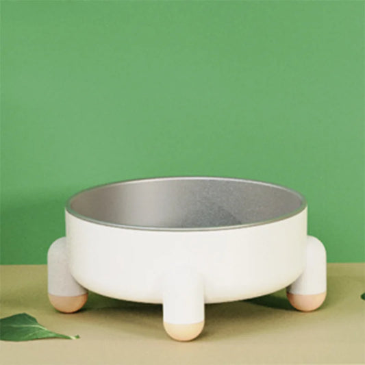 Gamelle pour chien en inox avec base blanche antidérapante à quatre pieds ronds, sur fond vert.