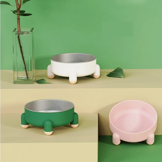 Trois gamelles en inox pour chien, posées sur une table, avec support antidérapant rose, blanc et vert foncé au design moderne.