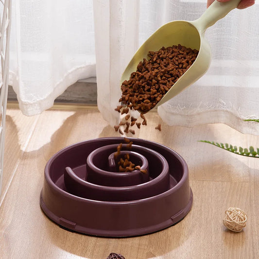 Gamelle spirale marron remplie de croquettes pour chien, avec une main versant les aliments.