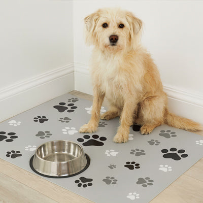 chien assis près d’une gamelle en inox posée sur un tapis gamelle pour chien gris avec motifs empreintes